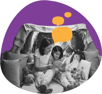 Female caregiver reading with young child in pillow fort.